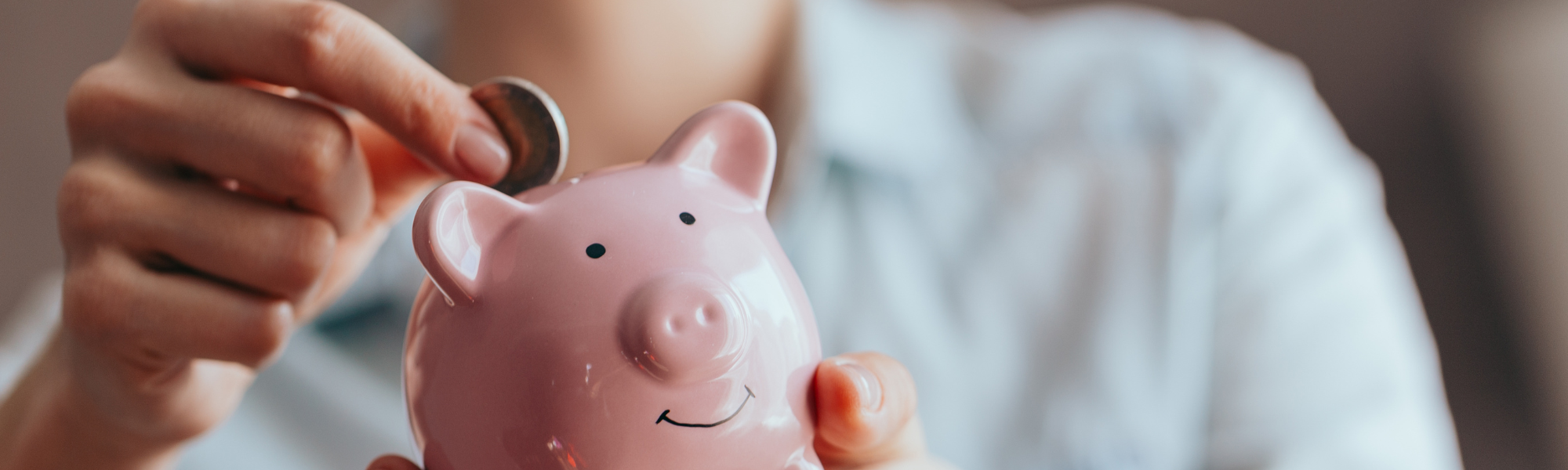 hand putting coin in to pink china piggy bank