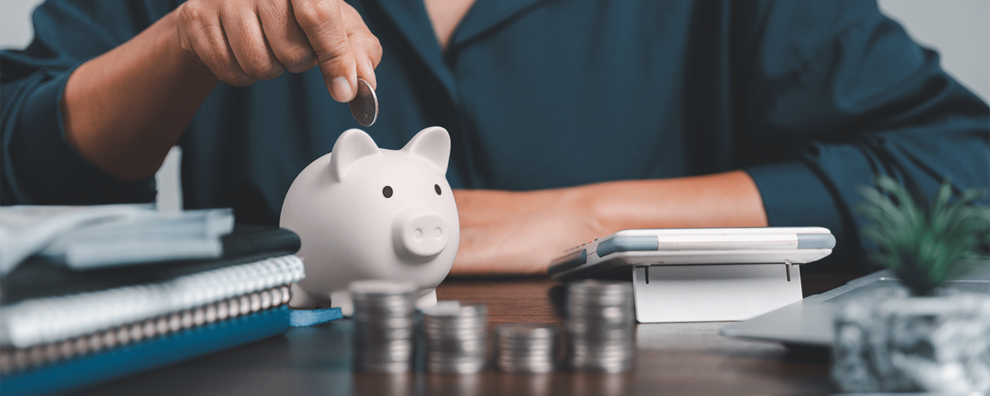 Man sitting at desk with a calculator and pink piggy bank inserting coins into the piggy bank